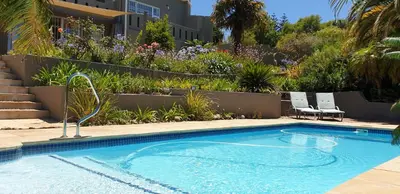 a swimming pool with two chairs and a garden at Agape Apartments in Somerset West