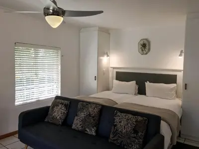 a bedroom with a bed with a couch and a ceiling fan at Howards End Manor B&B in Cape Town