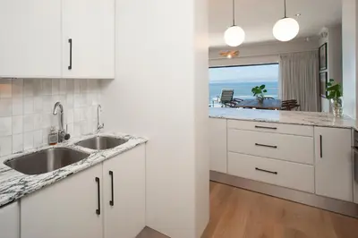 a kitchen with white cabinets and a view of the ocean at Hamewith Penthouse in Hermanus