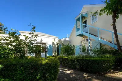 a white building with a blue railing and bushes at Auberge Clermont in Franschhoek
