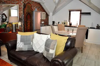 a living room with a leather couch and a kitchen at Los Olivos at the Yard in Franschhoek