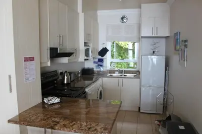 a kitchen with white cabinets and a white refrigerator at The Blue Marine Self-Catering in Gordonʼs Bay