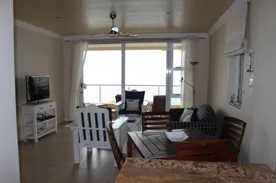 a living room with chairs and a couch and a television at The Blue Marine Self-Catering in Gordonʼs Bay