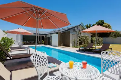 a pool with a table and chairs and umbrellas at Bloubergstrandlodge in Bloubergstrand
