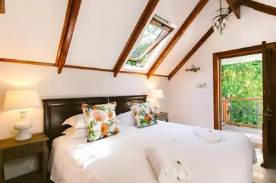 a bedroom with a bed with white sheets and a window at Roosenwijn Guesthouse in Stellenbosch