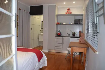 a bedroom with a bed and a desk and a kitchen at Anni Bos in Stellenbosch