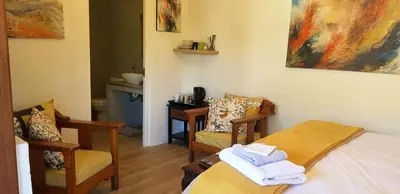 a bedroom with a bed and two chairs and a table at Hemel en Aarde Village Accommodation in Hermanus