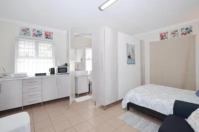 a white bedroom with a bed and a kitchen at Arum Field Accommodation in Table View