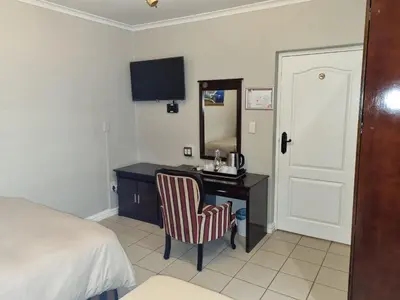 a bedroom with a desk with a chair and a mirror at Savoy Lodge in Cape Town
