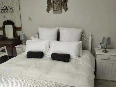 a white bed with two black pillows on it at Feet Up Cottage in Somerset West