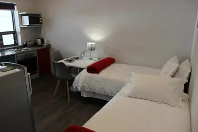 a room with two beds and a desk and a kitchen at Zeederberg Corner in Paarl