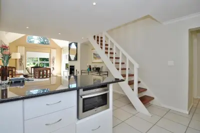 a kitchen with a staircase and a living room at Glen Abbey Apartments On The Erinvale Golf And Country Estate in Somerset West