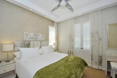 a bedroom with a large white bed and a ceiling fan at Glen Abbey Apartments On The Erinvale Golf And Country Estate in Somerset West
