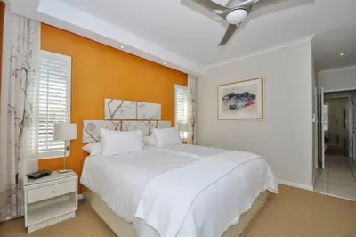 a bedroom with a large white bed and an orange wall at Glen Abbey Apartments On The Erinvale Golf And Country Estate in Somerset West