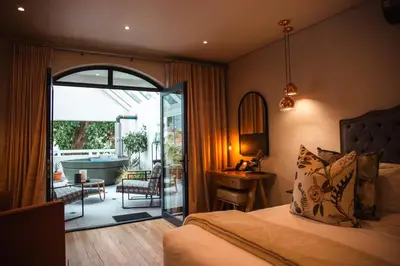 a bedroom with a bed and a balcony with a tub at Le Petit Manoir Boutique Hotel in Franschhoek