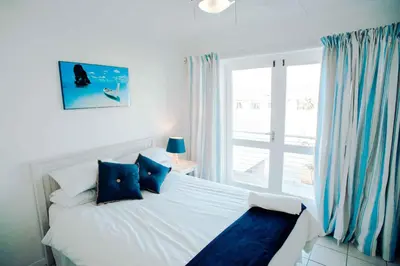 a bedroom with a bed with blue pillows and a window at 20 Cayman Beach, Gordon's Bay in Gordonʼs Bay
