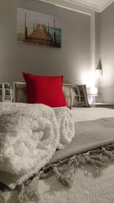 a bed with a white blanket and a red pillow at Hamilton Garden Suites in Parklands