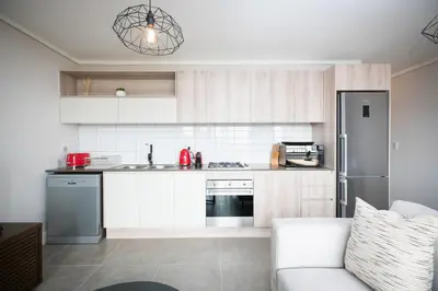a kitchen with white cabinets and a couch at Waters Edge Self-Catering Apartment in Cape Town