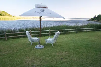 two chairs and an umbrella next to the water at Kennedys Beach Villa in Hermanus