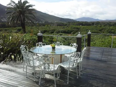 a glass table and chairs on a wooden deck at Kennedys Beach Villa in Hermanus