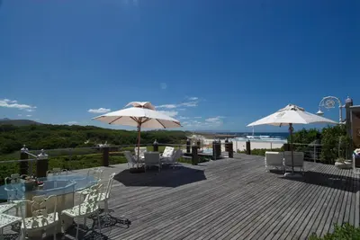 a deck with tables and chairs and umbrellas at Kennedys Beach Villa in Hermanus