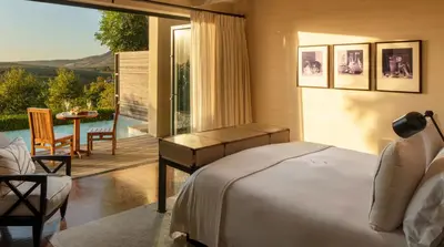 a bedroom with a bed and a balcony with a table at Delaire Graff Lodges and Spa in Stellenbosch