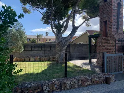 a fence with a tree in front of a house at The Yard in Gordonʼs Bay