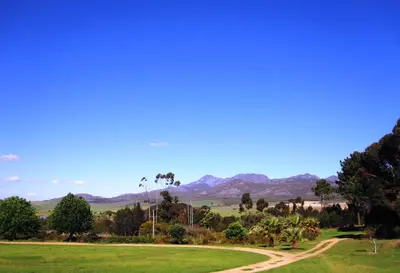 a grassy field with a dirt road and mountains in the background at The Cottage at Nuwejaarsrivier Farm in Kleinmond