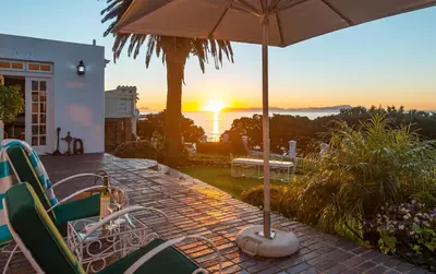 a patio with chairs and an umbrella and the sunset at Manor on the Bay in Gordonʼs Bay