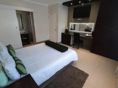 a bedroom with a large white bed and a desk at La Roche Guest House in Cape Town