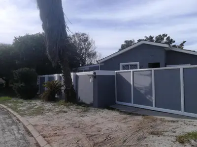 a blue house with a fence and a palm tree at Cape Pine Guest House in Kuilsrivier