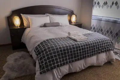 a bed with a black and white blanket and two lamps at Cape Pine Guest House in Kuilsrivier