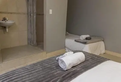 a bathroom with two beds and a shower and towels at Cape Pine Guest House in Kuilsrivier