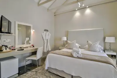 a white bedroom with a bed and a desk and a mirror at Hermanus Lodge on the Green - Solar Power in Hermanus