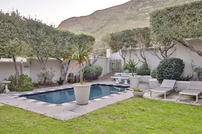 a backyard with a swimming pool with chairs and trees at Hermanus Lodge on the Green - Solar Power in Hermanus