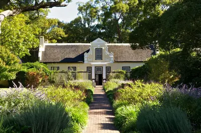 a white house in the middle of a garden at Golden Hill Guest House in Somerset West