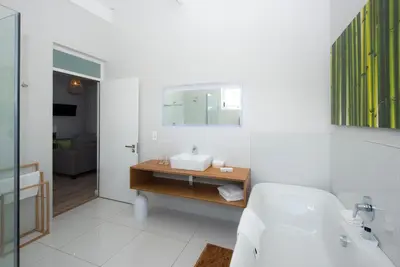a white bathroom with a sink and a mirror at Bamboo Guest House in Hermanus