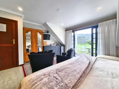 a bedroom with a large bed with chairs and a window at Mulligans Guest Lodge in Hermanus