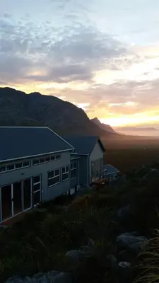a house on a hill with the sunset in the background at Tranquility Heights in Pringle Bay