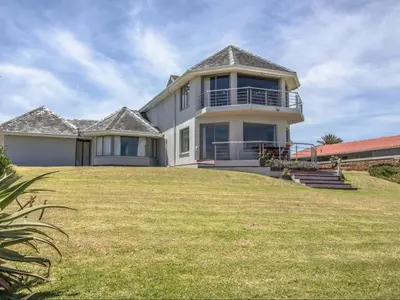 a large house on top of a grassy hill at Sandbaai Country House in Hermanus