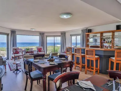 a living room with a bar and the ocean at Sandbaai Country House in Hermanus