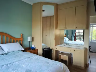a bedroom with a bed and a desk with a mirror at Lemon Tree Cottage in Edgemead