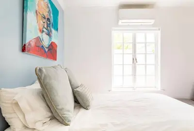 a bedroom with a white bed with a painting on the wall at Art House in Stellenbosch