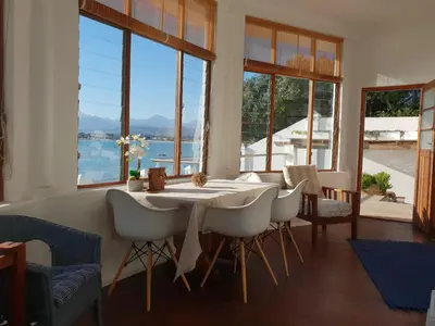a dining room with a table and chairs and windows at Westbank Private Beach Villa, 4 Bedrooms, Private pool, on the Beach! in Gordonʼs Bay