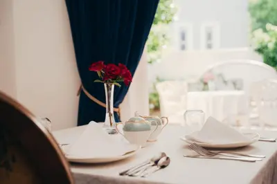 a table with plates and a vase of roses on it at Les Chambres Guest House in Franschhoek