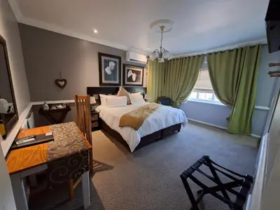 a bedroom with a bed and a table and a desk at Leeuwenhof Guesthouse in Caledon