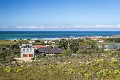 a house on a hill with the ocean in the background at The Trailhouse - Betty's Bay in Bettyʼs Bay