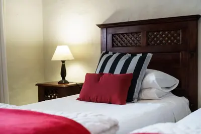 a bed with a wooden headboard and a red pillow at Be My Guest Lodge in Bloubergstrand