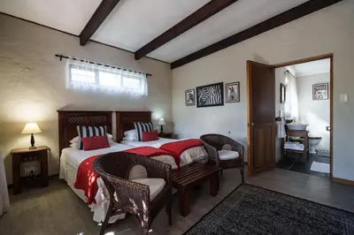 a bedroom with a bed with a red blanket and chairs at Be My Guest Lodge in Bloubergstrand