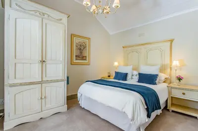 a bedroom with a large white bed and a chandelier at Franschhoek Rose Cottages in Franschhoek